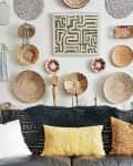 Eclectic living room with woven wall decor, abstract art, and a black leather sofa adorned with patterned and textured pillows.