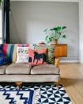 Beige sofa with colorful cushions, geometric rug, and a potted plant on a wooden sideboard in a modern living room.
