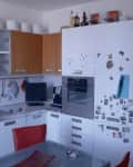 Small kitchen with white cabinets, wooden accents, red chairs, and fridge covered in magnets.