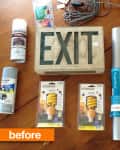 Materials for DIY project: EXIT sign, spray paint, light bulbs, ruler, screwdriver, cords, and contact paper on a wooden table.