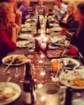Dinner party with people seated around a long table, enjoying food and drinks, with candles and autumn decor.