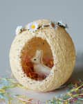 Woven egg-shaped basket with daisies, holding a white rabbit figurine and colorful shredded paper.