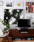 Mid-century modern living room with a dark wood TV stand, floral wall art, framed prints, and a potted plant.