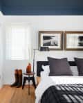 Cozy bedroom with dark pillows, framed art, bedside table, lamp, and boots by the window.