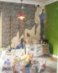 Room under renovation with peeling wallpaper, green walls, and construction materials scattered on the floor.