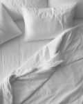 Unmade bed with white sheets and pillows, featuring a crumpled duvet.