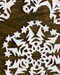 Paper snowflakes with intricate star and geometric patterns on a wooden surface.