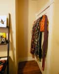 Narrow hallway with scarves hanging on a door and a shelf with books and a mug.