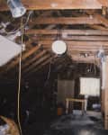 Unfinished attic with exposed wooden beams, wires, and a small window.