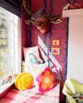 Colorful room corner with patterned wallpaper, decorative pillows, a mounted deer head, and small framed art pieces.