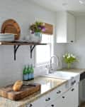 Galley kitchen with granite countertops, white cabinets, open shelves, bread on cutting board, and flowers by the sink.