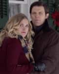 A couple standing outside a house decorated with Christmas garland and red poinsettias.