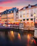 Colorful buildings and boats along Nyhavn canal in Copenhagen at sunset, with vibrant sky and reflections in the water.