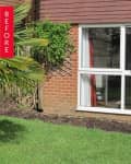 Brick house exterior with large windows, red curtains, and garden plants.