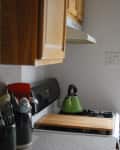 Kitchen counter with utensils in black holders, a green kettle on the stove, and wooden cabinets above.