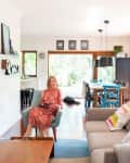 Woman in red dress sitting on a blue chair in a bright living room with modern decor and wooden dining table.