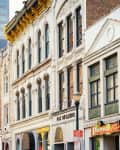 Historic downtown street with ornate brick buildings, including Shiraz Grill, under a clear sky.