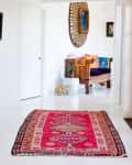 Hallway with a vibrant red patterned rug, wooden bench with colorful cushions, and a large decorative mirror.