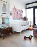 Nursery with white crib, wooden side table, colorful toys, wall art, and a large window with natural light.