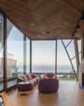 Oceanfront living room with large windows, pink sofas, modern fireplace, and wooden ceiling.