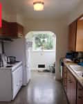 Narrow kitchen with white appliances, wooden cabinets, and a window with bunting.