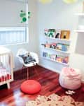 Nursery with wooden floor, white crib, bookshelves, a chair with a panda cushion, and yellow hanging pom-poms.