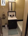 Small bathroom with black vanity, mirror, white sink, and black-and-white tile floor. Beige walls and towel rack.