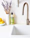 A clean, white sink with a hand soap and small flower vase on the left of the faucet and bottles of olive oil and balsamic vinegar on the right