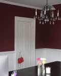 Dining room with dark red walls, white trim, a black chandelier, and a dark table with flowers and a candle.
