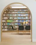 Arched entryway leading to a library with color-coordinated bookshelves, a table, and four dark green chairs.