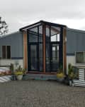 Modern tiny house with large glass doors, metal siding, and potted plants on a gravel driveway.