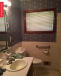 Bathroom with floral wallpaper, white sink, toilet, grab bar, and blinds on window.