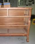 Wooden dresser frame with two shelves and curved legs in a workshop setting.