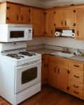 Wooden kitchen cabinets with black handles, white stove, microwave, and paper towel holder above the sink.