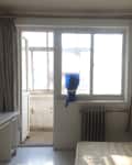 Bedroom with large window, radiator, TV on desk, and beige curtains.