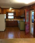 Wood-paneled kitchen with white fridge, green stove, red door, and tiled floor.