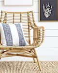Rattan chair with a striped cushion, white side table, and framed art on shiplap wall.