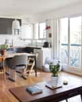 Open-plan kitchen and dining area with wooden floors, modern chairs, potted plants, and large windows leading to a balcony.