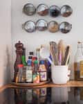 Kitchen counter with spice rack, condiments, utensils in a white holder, and a bottle of oil.