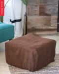 Brown ottoman with a textured cover next to a teal sofa and rustic wooden wall.