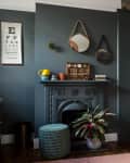 Dark gray living room with decorative fireplace, round mirrors, eye chart, potted plant, and bookshelf with books and decor.