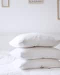 Three white pillows stacked on a neatly made bed with minimalistic wall decor.