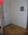 Small entryway with white door, wooden floor, wall hooks, and a gray electrical panel.