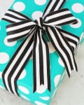Turquoise gift box with white polka dots, wrapped with a black and white striped ribbon bow.