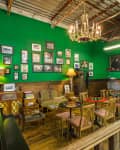 Vintage-style cafe with green walls, wooden furniture, framed photos, chandelier, and a small bar area.