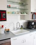 Modern kitchen with white cabinets, red microwave, glass shelves, coffee maker, and subway tile backsplash.