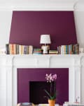 Living room with purple accent wall, white fireplace, books, orchid, and framed art. Two blue chairs flank the fireplace.