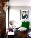 Cozy living room with a modern chair, ottoman, green dresser, and a framed portrait on the wall.