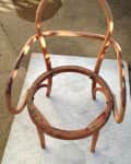 Wooden chair frame with curved arms and backrest, missing seat, on a textured surface.