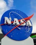 NASA logo on a blue sign with a red swoosh, set against a cloudy sky.